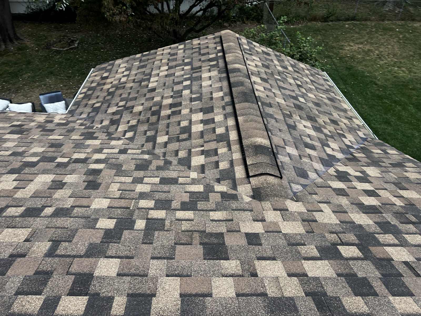 Overhead view of a completed multi-tone architectural shingle roof, the hip cap running up the corner and the gutter visible along the far eave